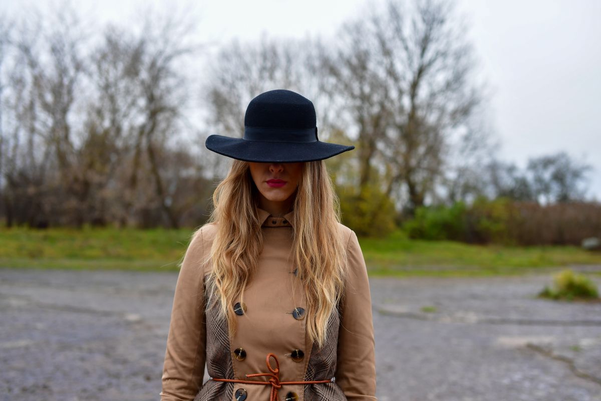 A fashionable woman in a trench coat and hat standing outdoors in Jägala-Joa, Estonia during fall.