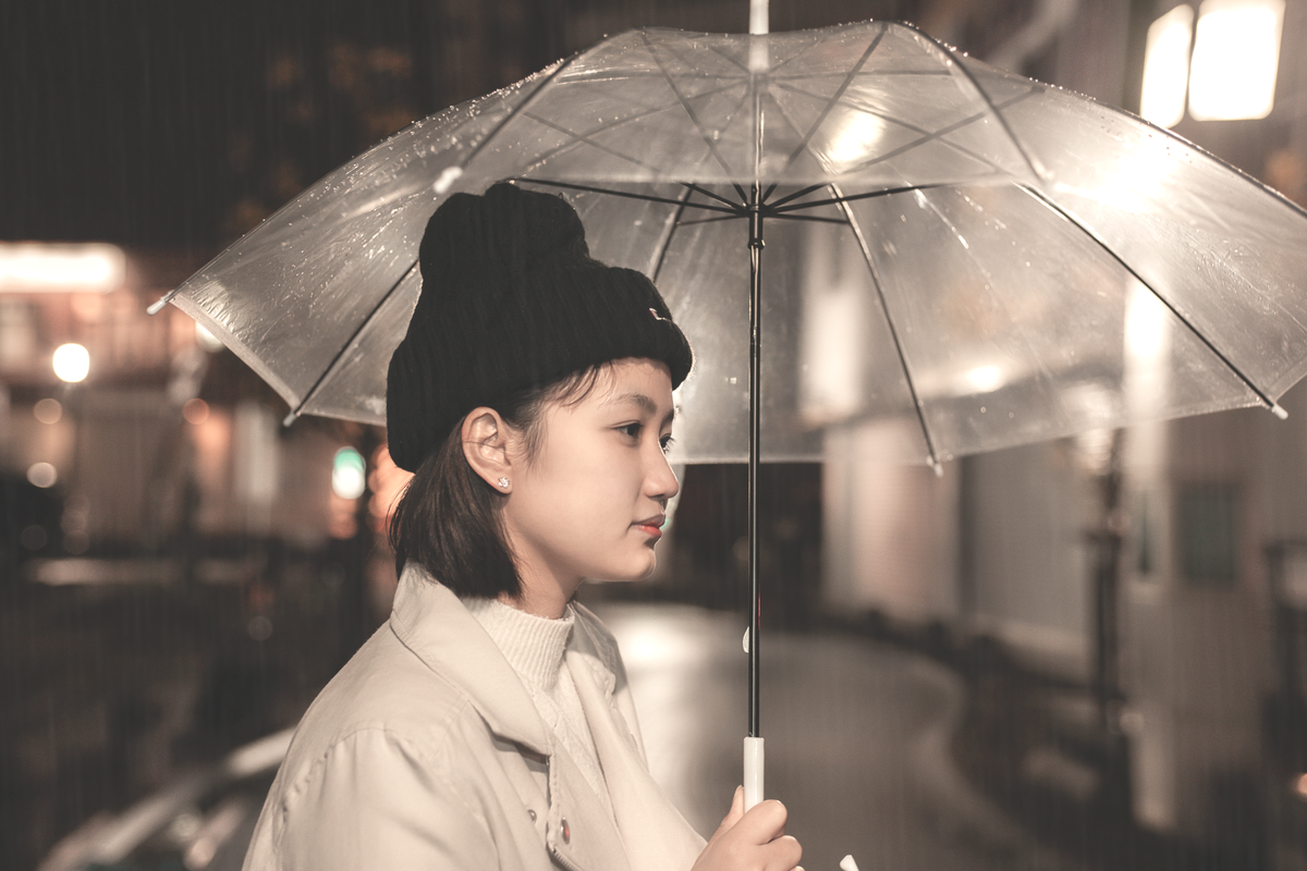 Side profile of a woman holding a clear umbrella during a rainy night on the street.