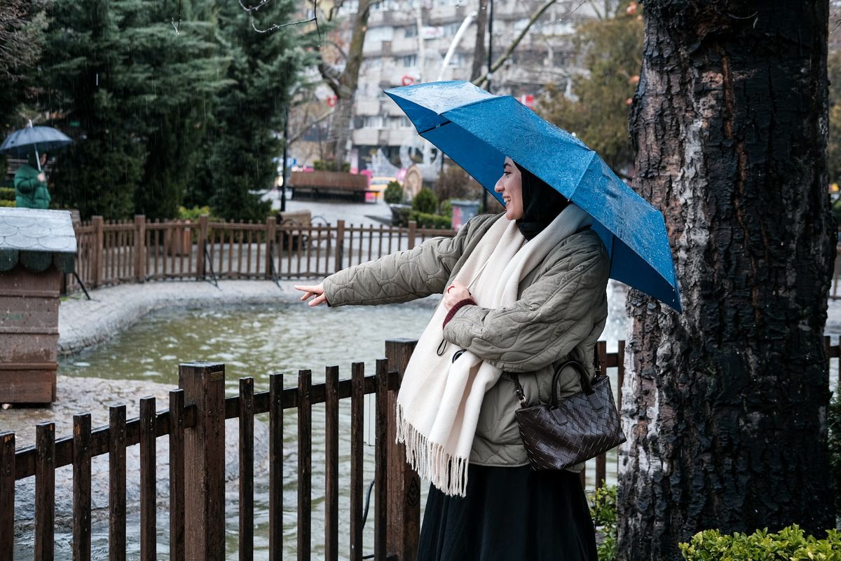 A woman holding a blue umbrella smiling by the pond on a rainy day.