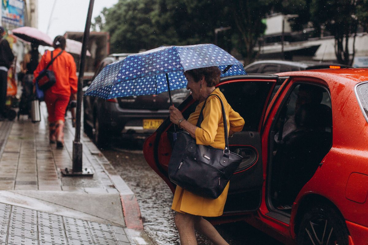 Woman with an umbrella getting out of a red car on a rainy day in the city.