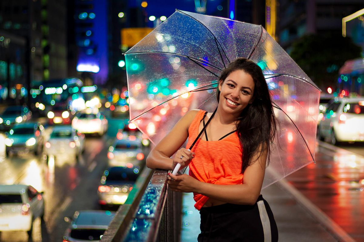 A woman smiles under a clear umbrella on a rainy night city street surrounded by vibrant lights.