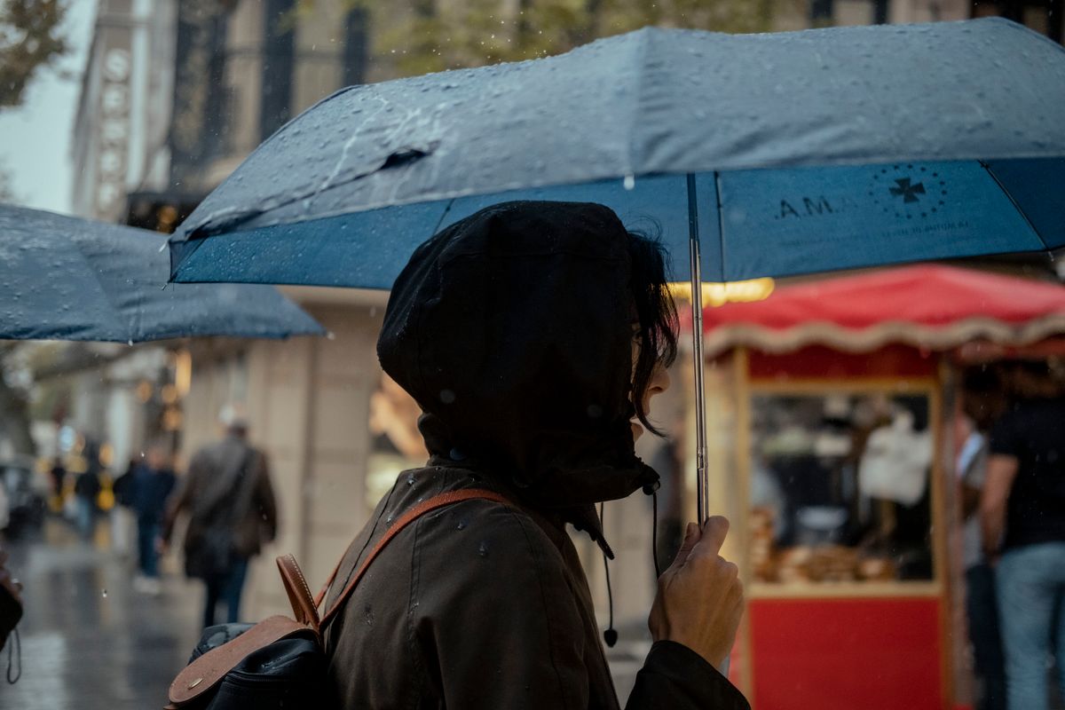 Side view of a woman holding an umbrella, standing in a rainy street, capturing a moment in urban life.
