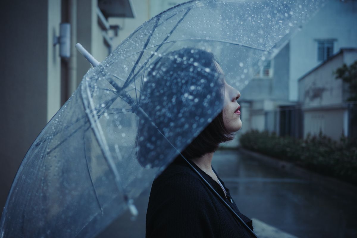 Side view portrait of a woman holding a transparent umbrella in a rainy urban setting, conveying a moody atmosphere.