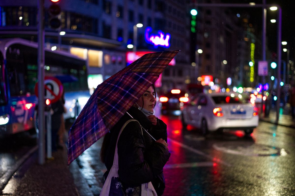 A woman holding an umbrella on a bustling city street during a rainy night.