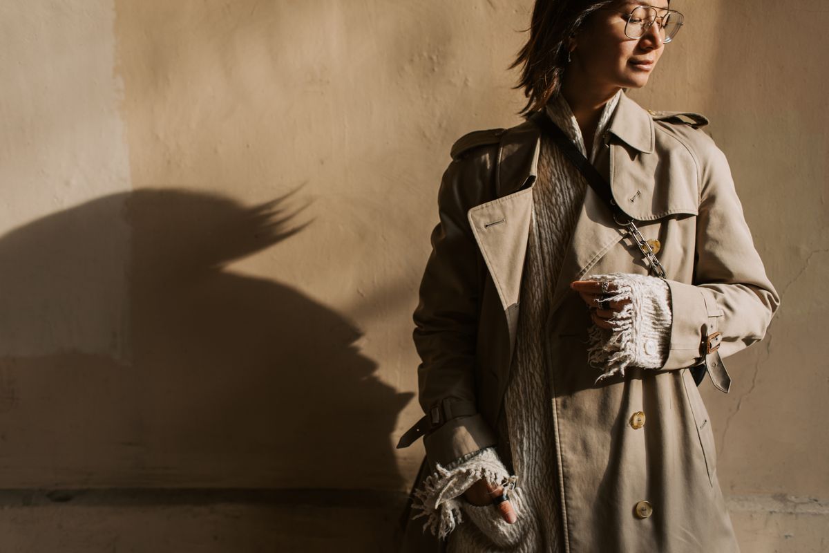 Fashionable woman in a trench coat posing with dramatic shadows in the fall sun.