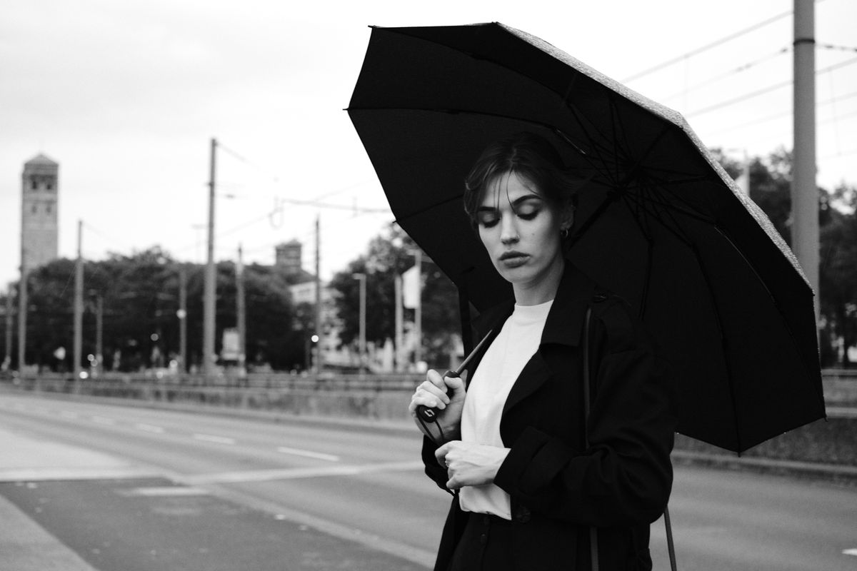 A fashionable woman holding an umbrella on a rainy day in Cologne's city streets.