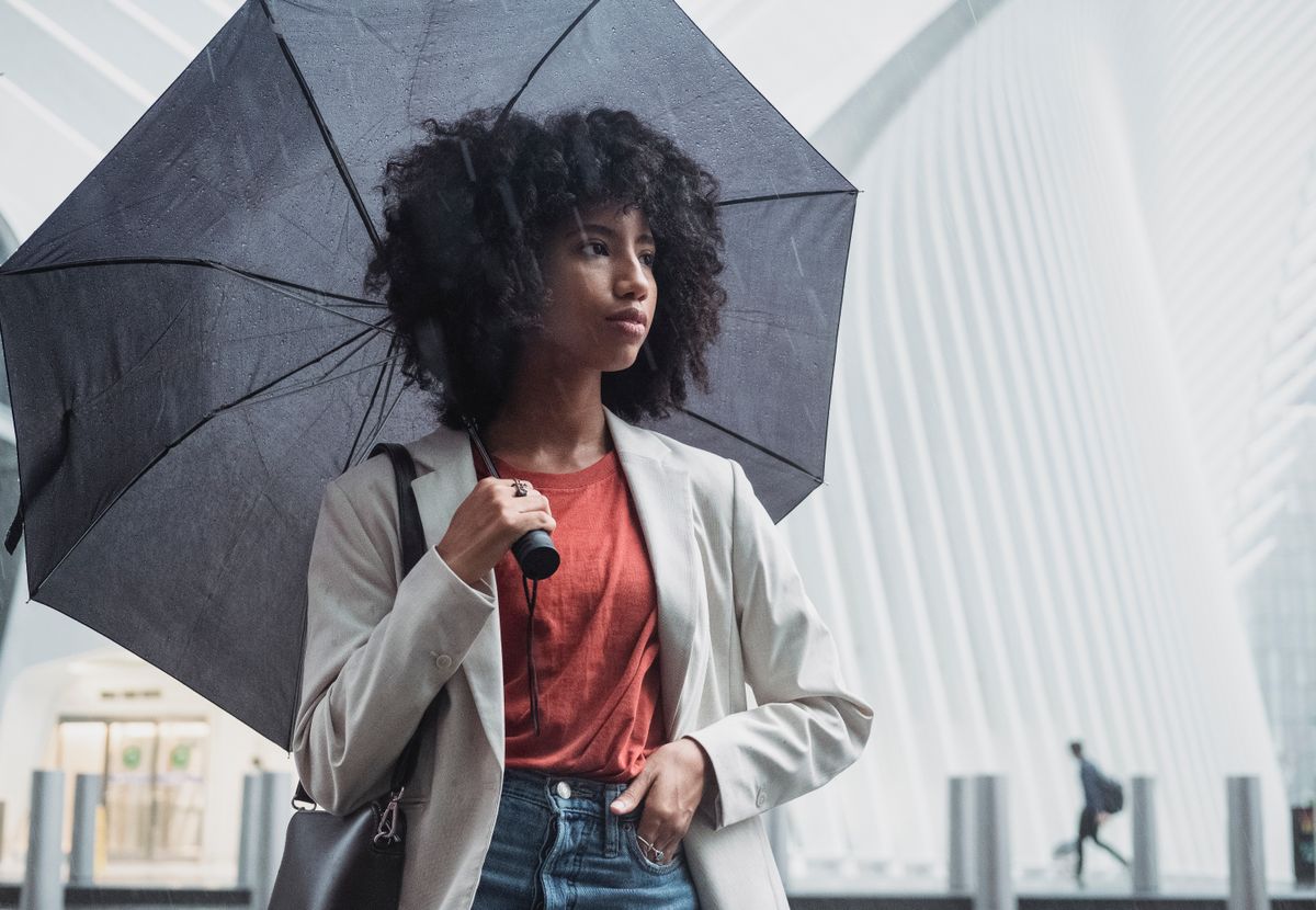 Woman standing under umbrella on a rainy day in an urban setting.