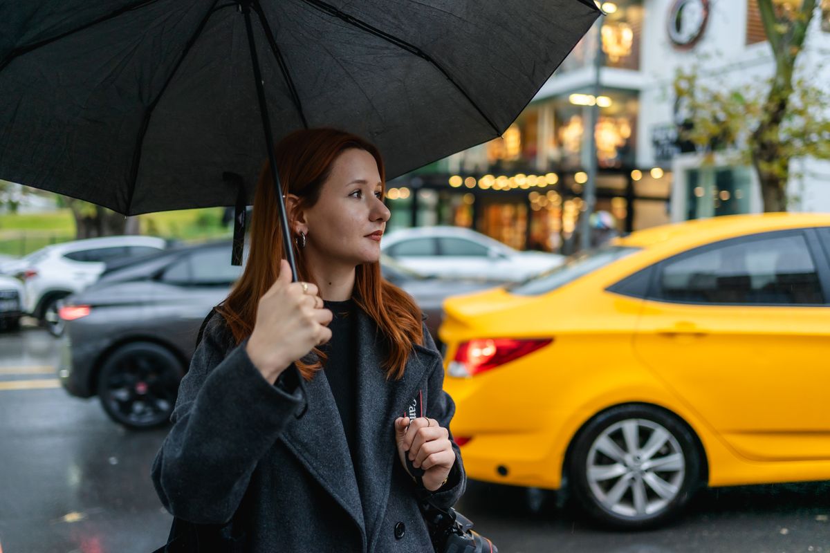 Red-haired woman with umbrella on a rainy day in Ankara, standing by city traffic.