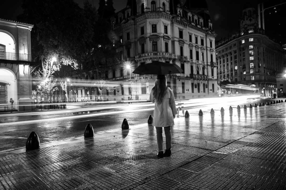 A woman with an umbrella stands on a rainy street at night in Buenos Aires.