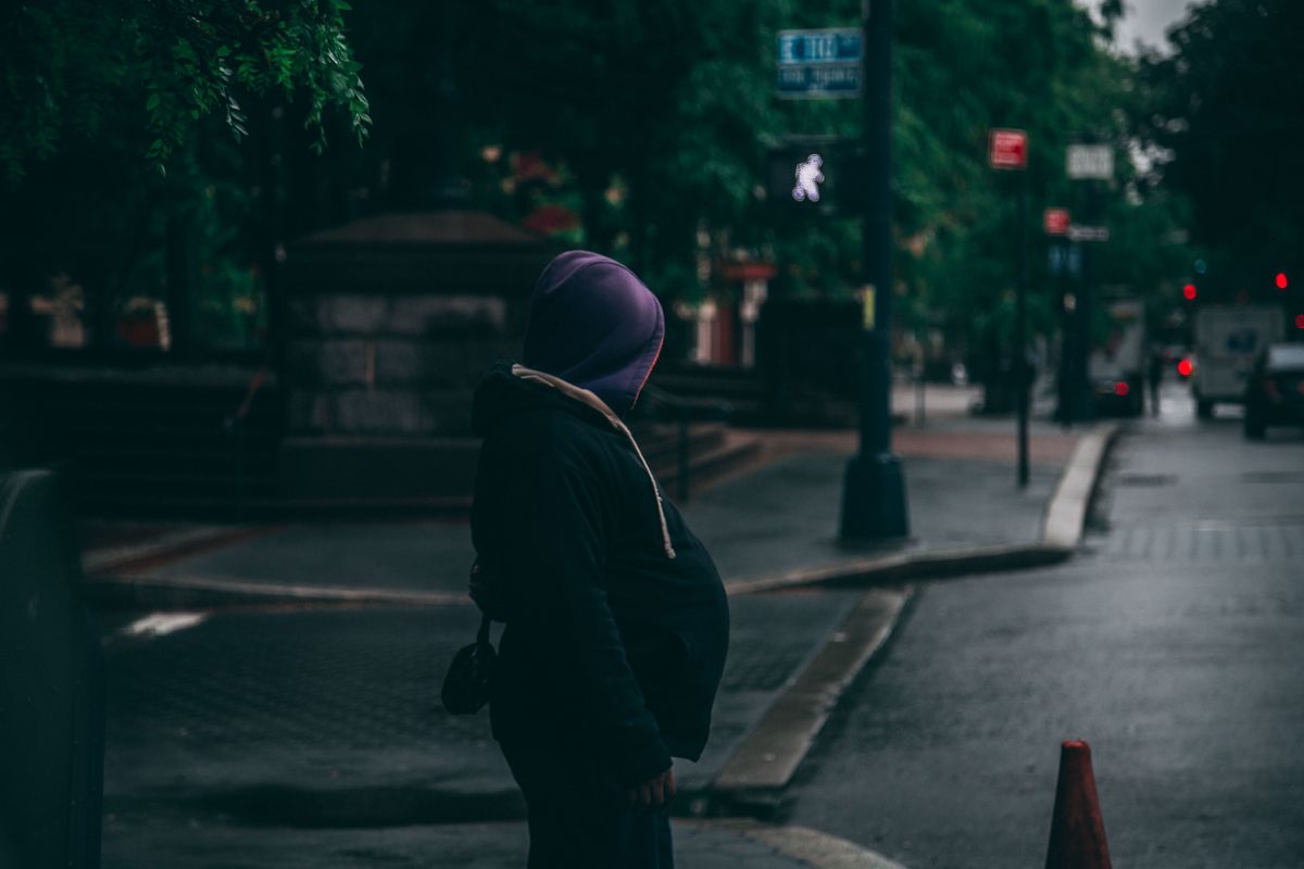 A mysterious figure in a hoodie stands in a rainy urban environment, evoking a sense of solitude.