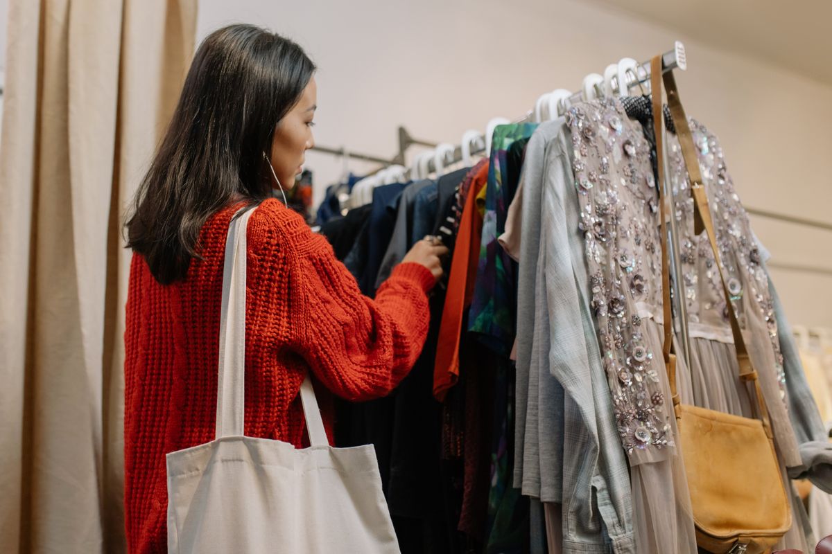 A woman browses a clothing rack in a cozy thrift shop, selecting garments.
