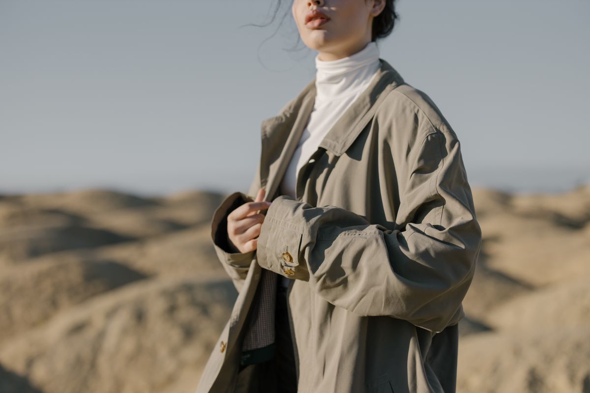 Stylish woman wearing a trench coat stands confidently in a wide desert landscape.