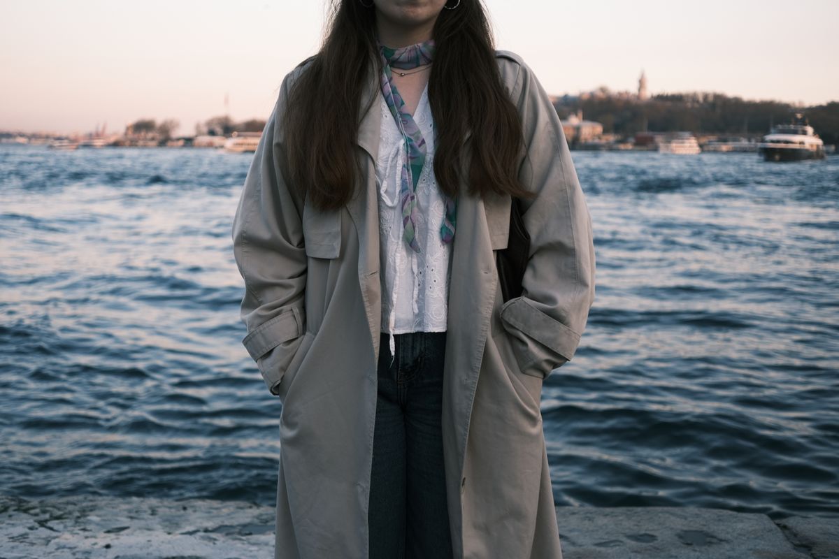 Stylish woman in trench coat standing by the waterfront during sunset.