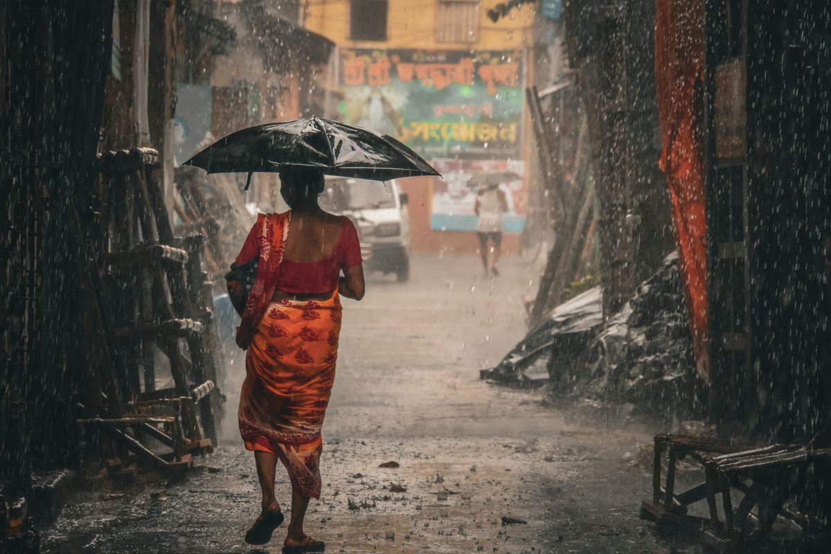 A woman in a sari walks with an umbrella through a rain-soaked alley in Kolkata, India.