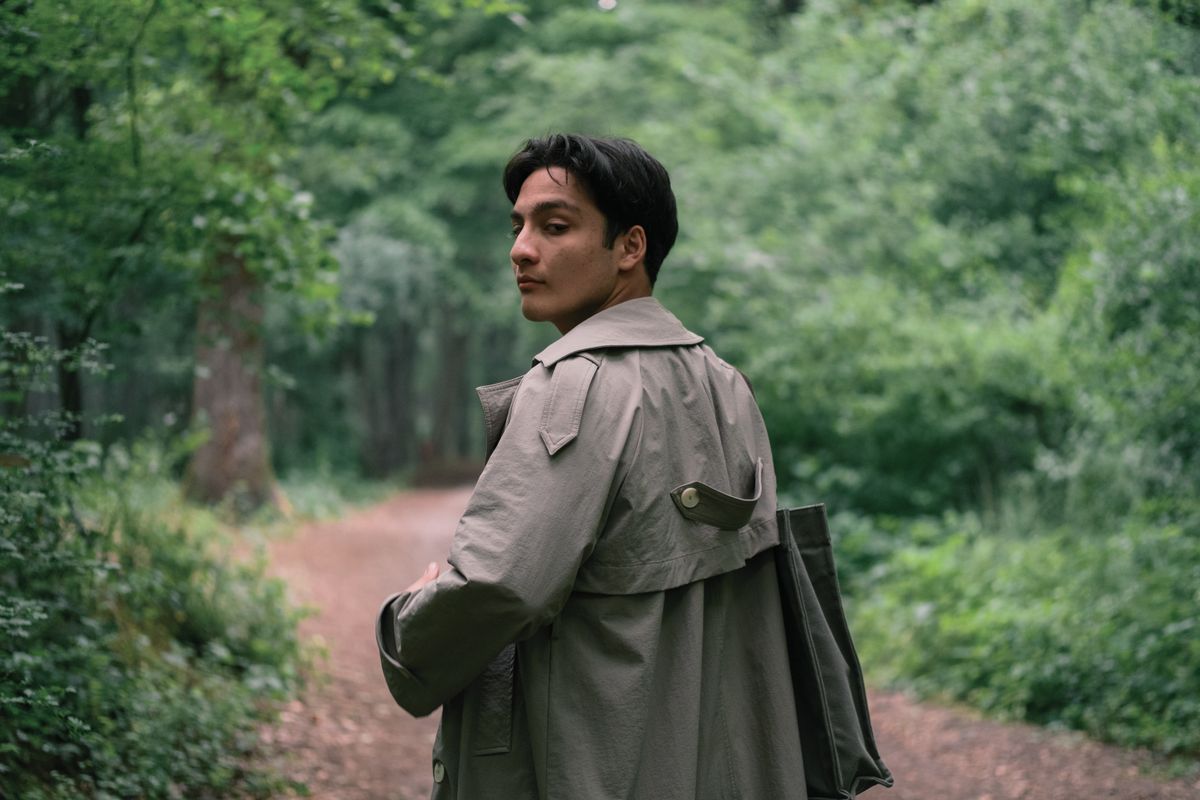 A contemplative scene of a man in a trench coat walking through a lush green forest.