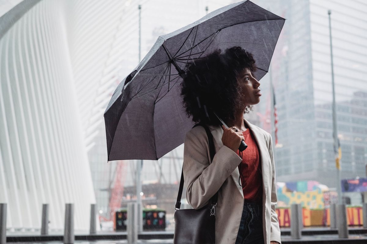 A woman stands with an umbrella under a rainy city sky, capturing urban life.