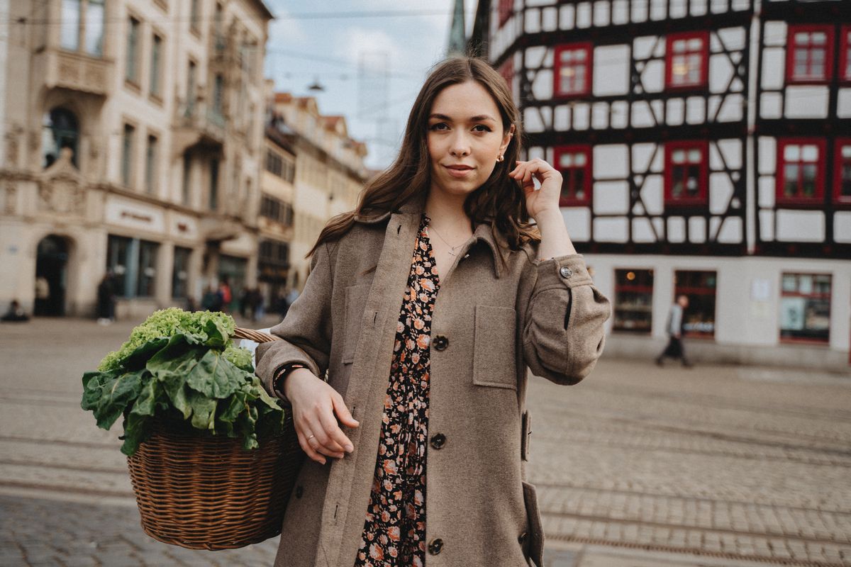 Woman in trench coat with vegetable basket exploring Erfurt's market square.