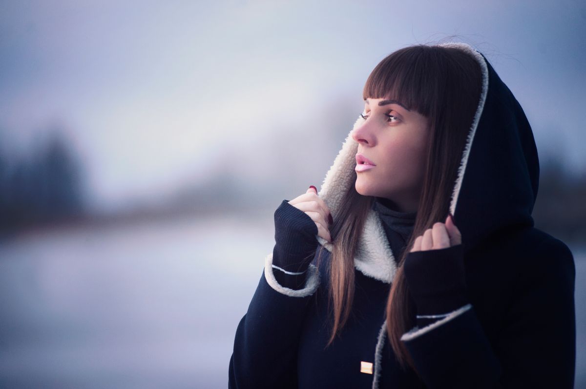 Stylish woman in a winter coat looking thoughtfully into the distance outdoors.