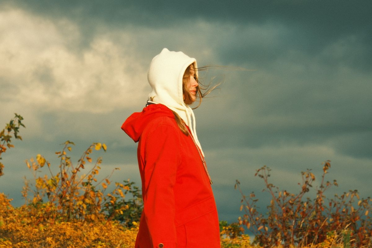 Woman in red coat with hood outdoors under dramatic stormy sky.