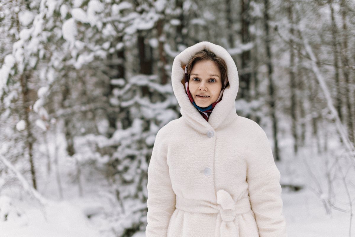 A woman in a white winter coat standing in a snowy forest, exuding warmth and style.