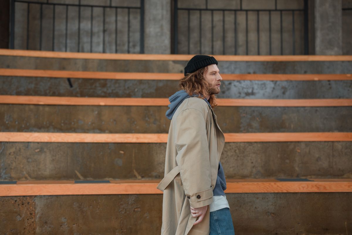 Side view of an adult man in a beige coat and beanie walking outdoors on bleachers.