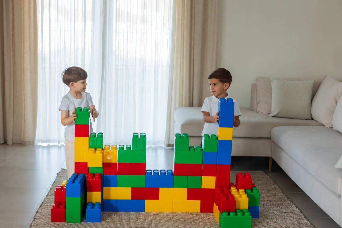 Two kids playing with large colorful building blocks in a living room setting, fostering creativity and teamwork.