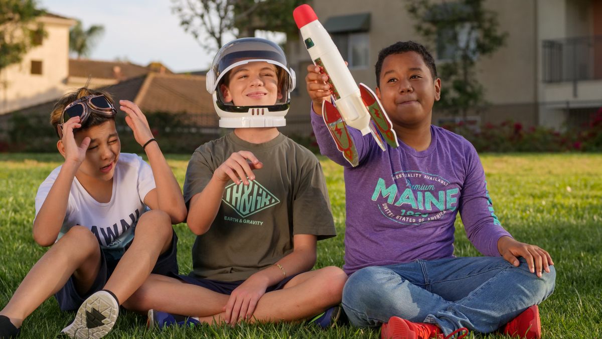 Three boys playing outdoors with a toy rocket, enjoying a sunny day.