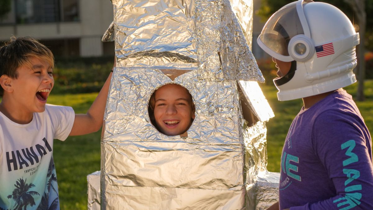 Three kids joyfully play with a homemade rocket, exploring space adventures.