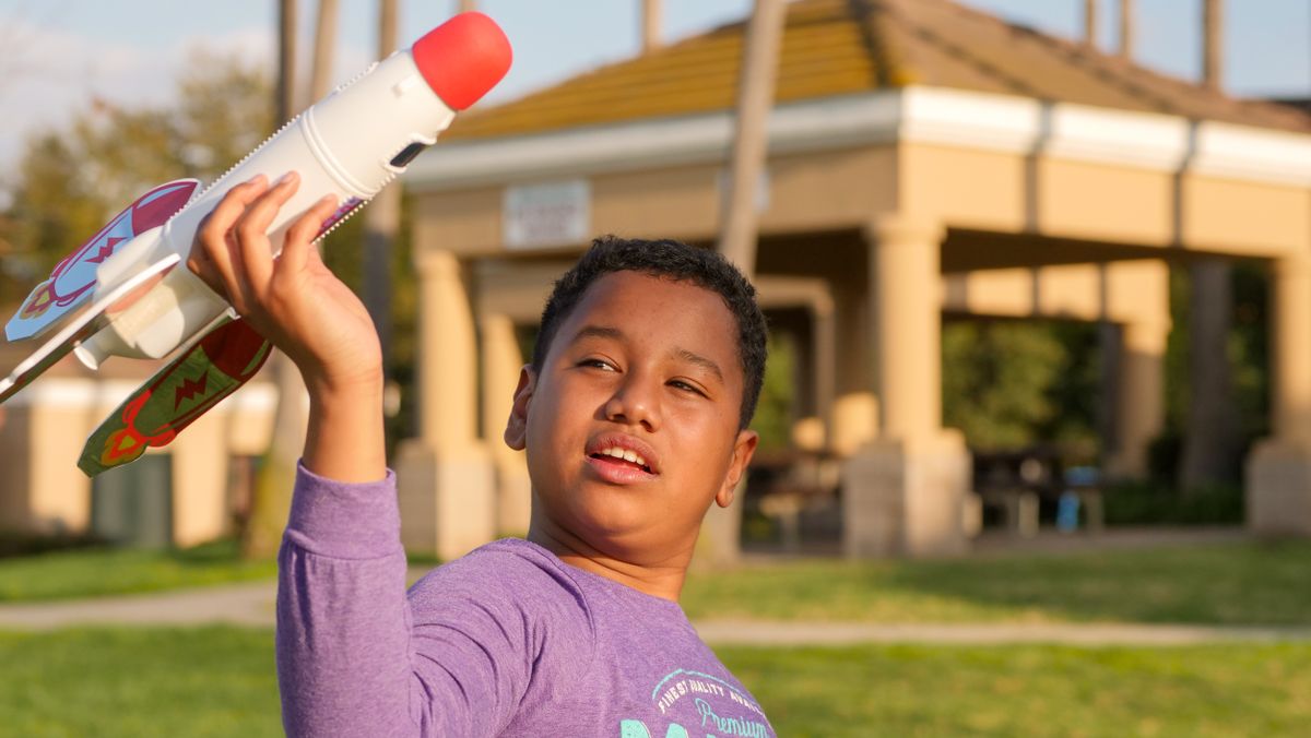 Child joyfully playing with a toy rocket in a sunny park setting.