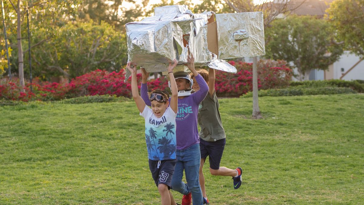 Children joyfully playing with a homemade cardboard rocket outdoors on a sunny day.