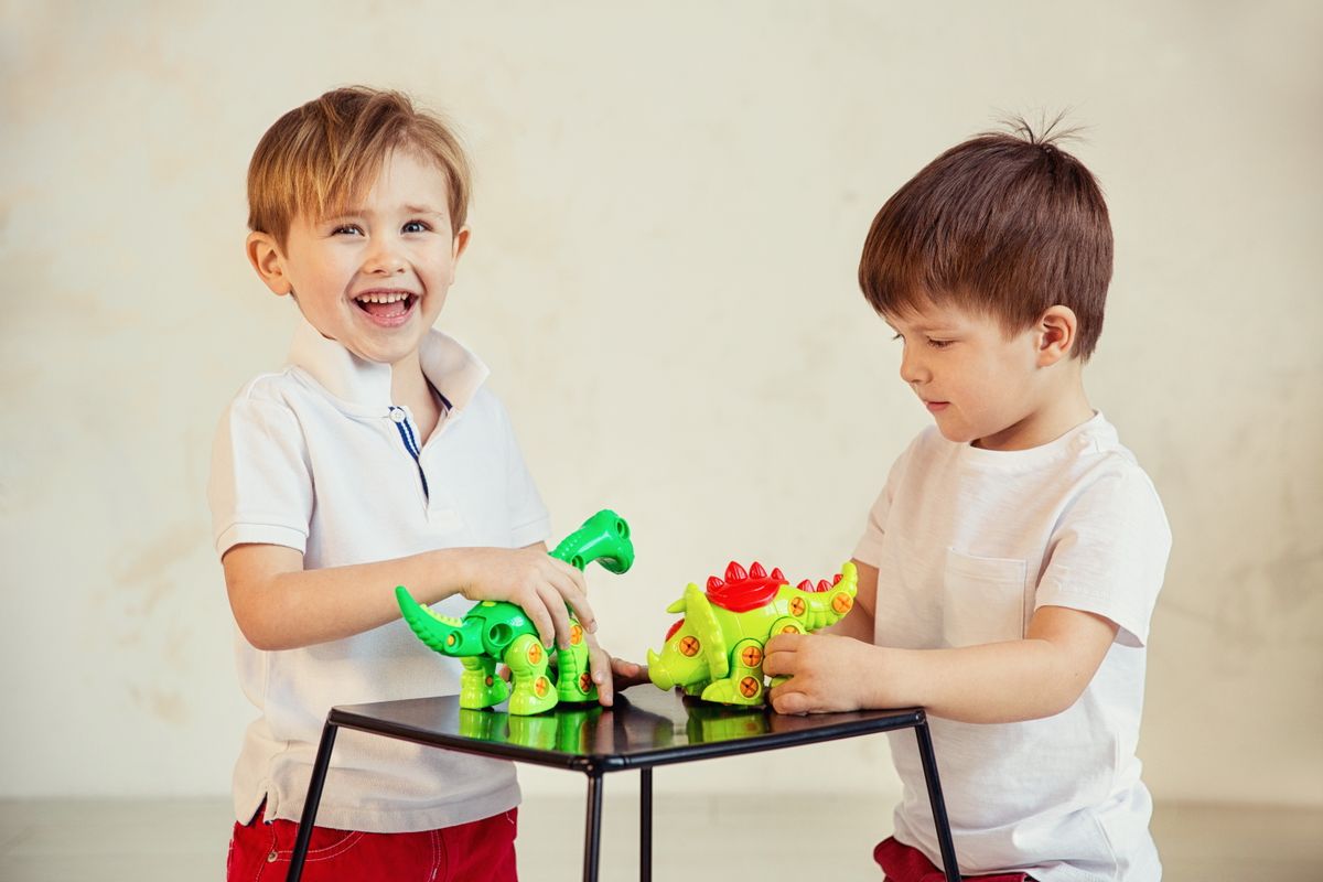 Two young boys having fun playing with colorful dinosaur toys at home.