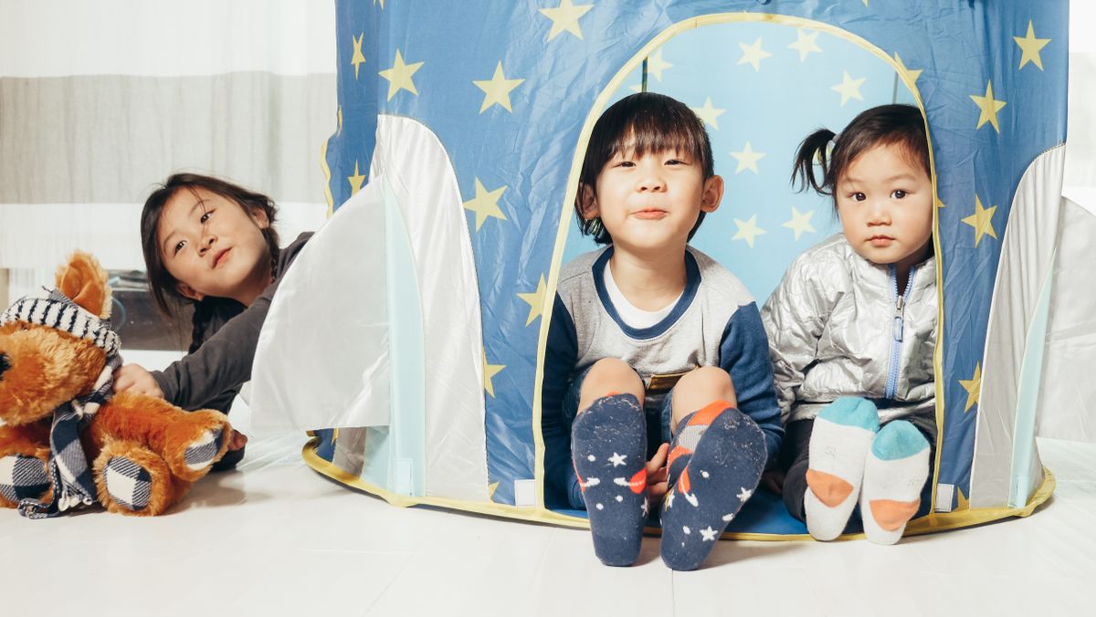 Three children sitting in a star-patterned tent enjoying playtime with toys.