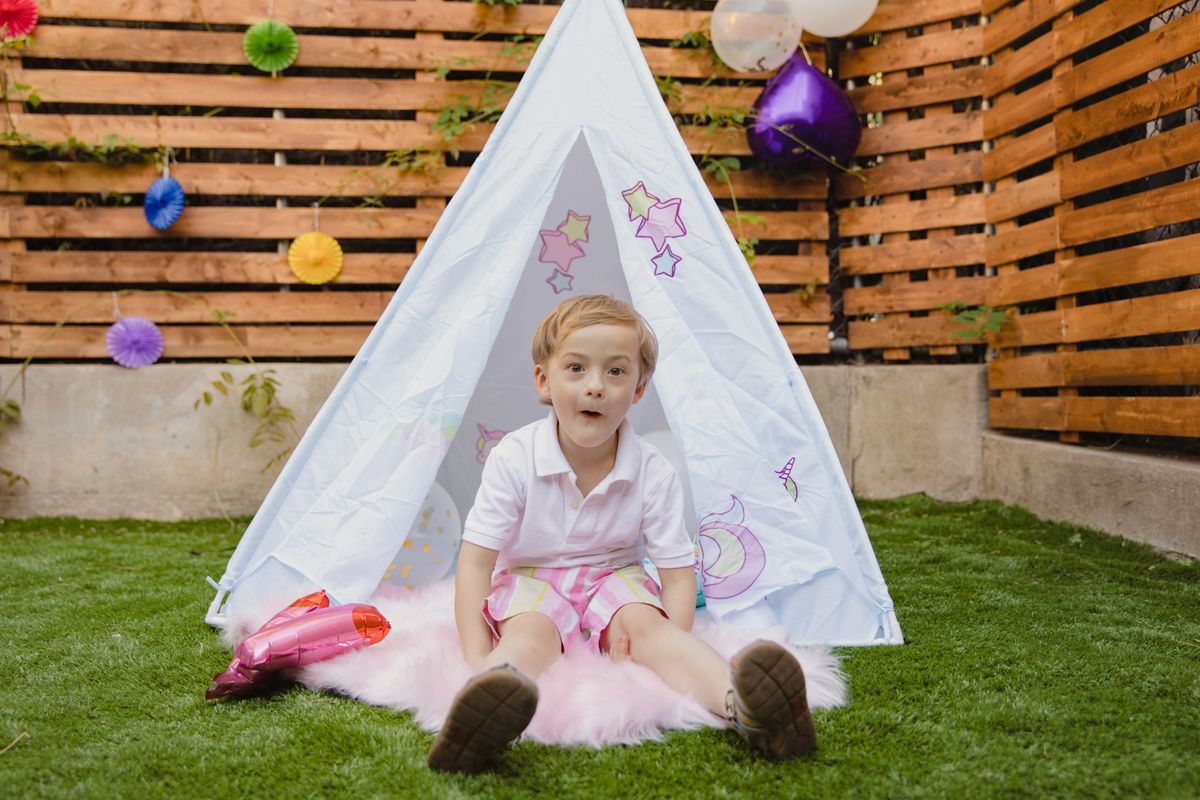 A joyful child enjoying a birthday party outdoors with colorful decorations and a play tent.