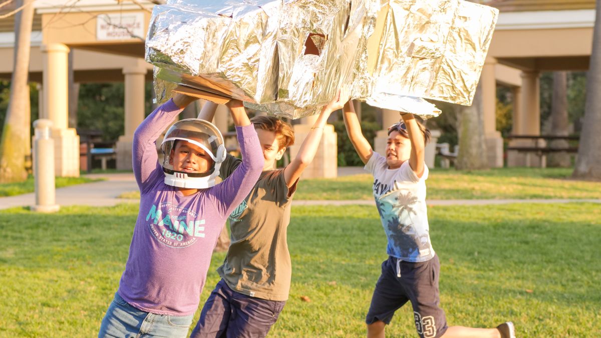 Kids playing with a cardboard rocket outdoors, fostering creativity and teamwork.