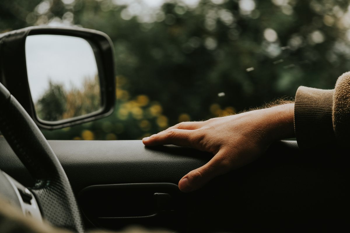 A serene view of a hand resting on a car door inside a parked vehicle surrounded by nature.