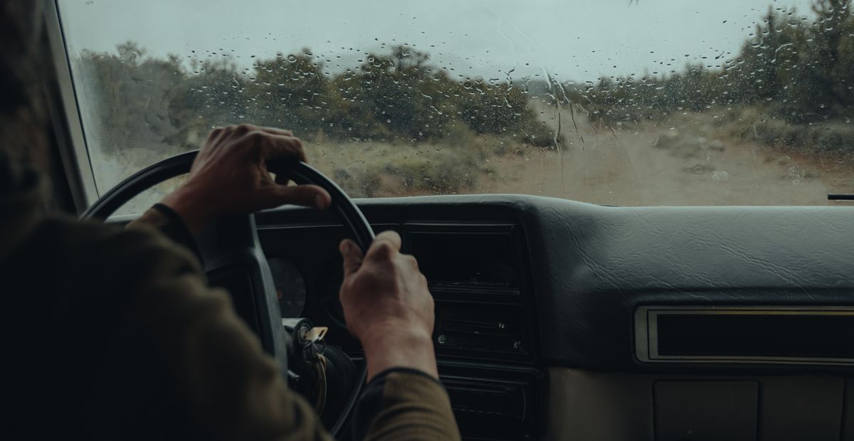 View from inside a vehicle driving off-road on a rainy day with raindrops on the windshield.