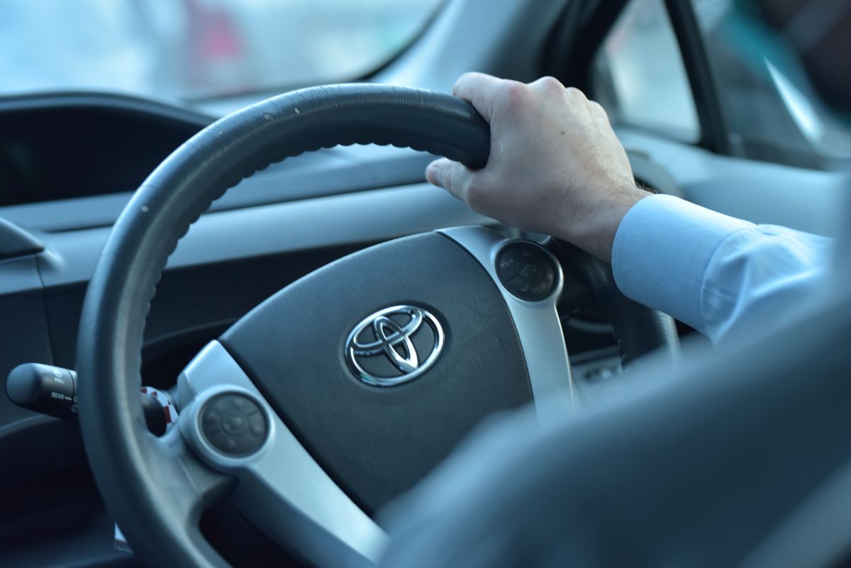 Close-up view of a hand gripping a Toyota steering wheel in a car interior, Faisalabad, Pakistan.