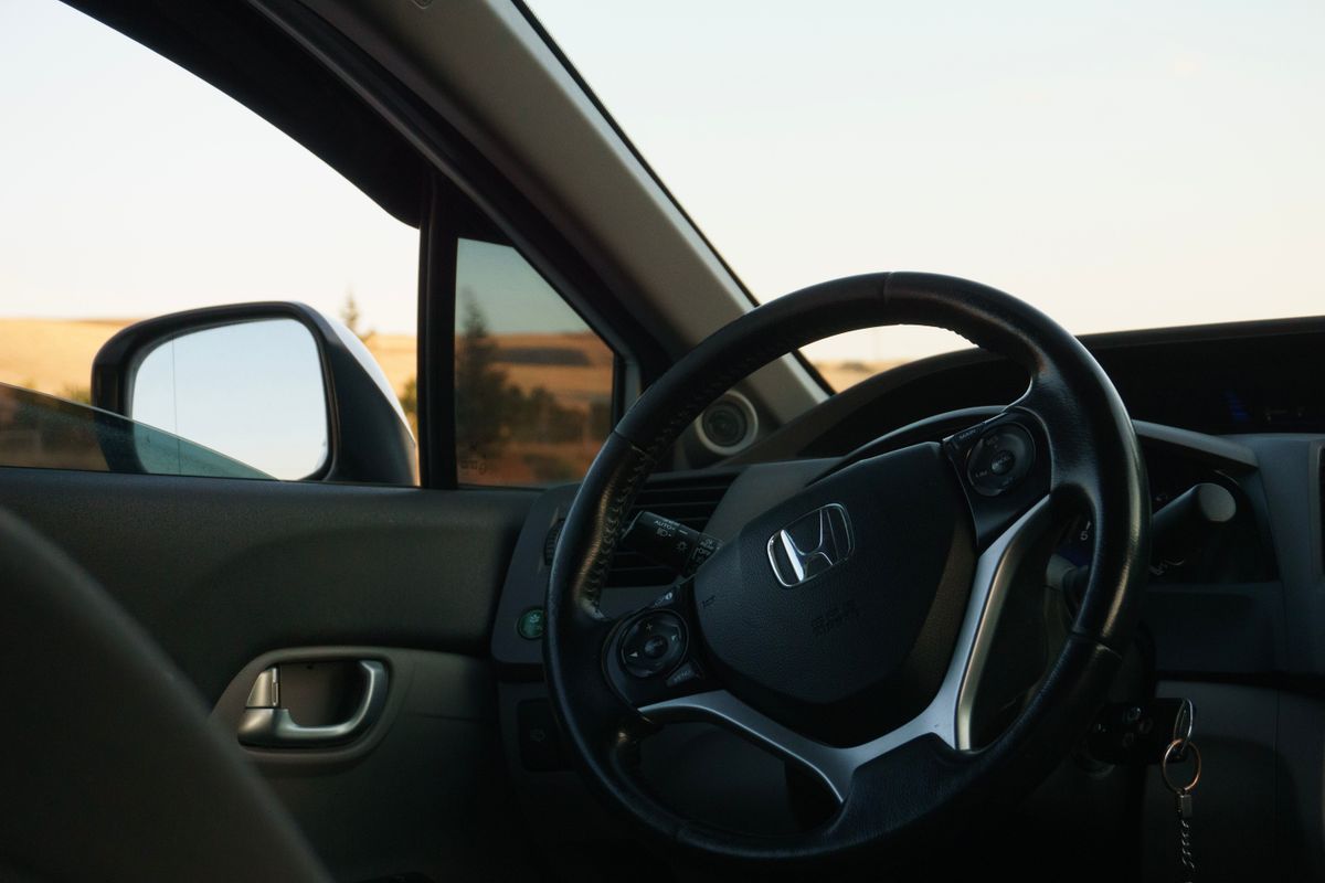 Close-up of a car steering wheel with dashboard and window view, embodying luxury and travel.