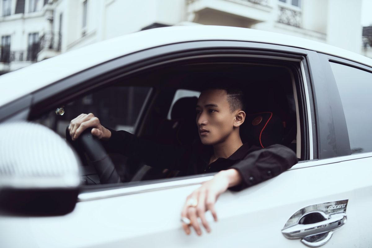 Side view of young concentrated Asian male millennial with cigarette in hand driving modern car in city