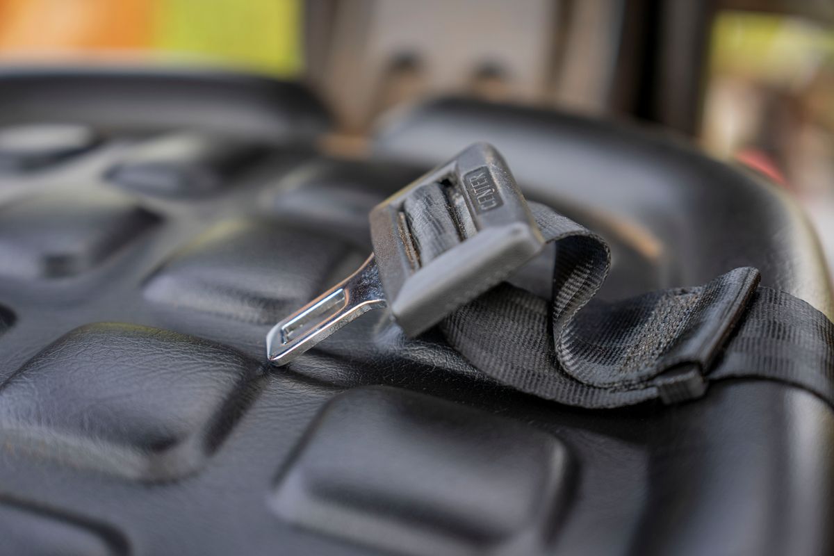 Detailed macro shot of a metal seatbelt buckle on a textured black vehicle seat.