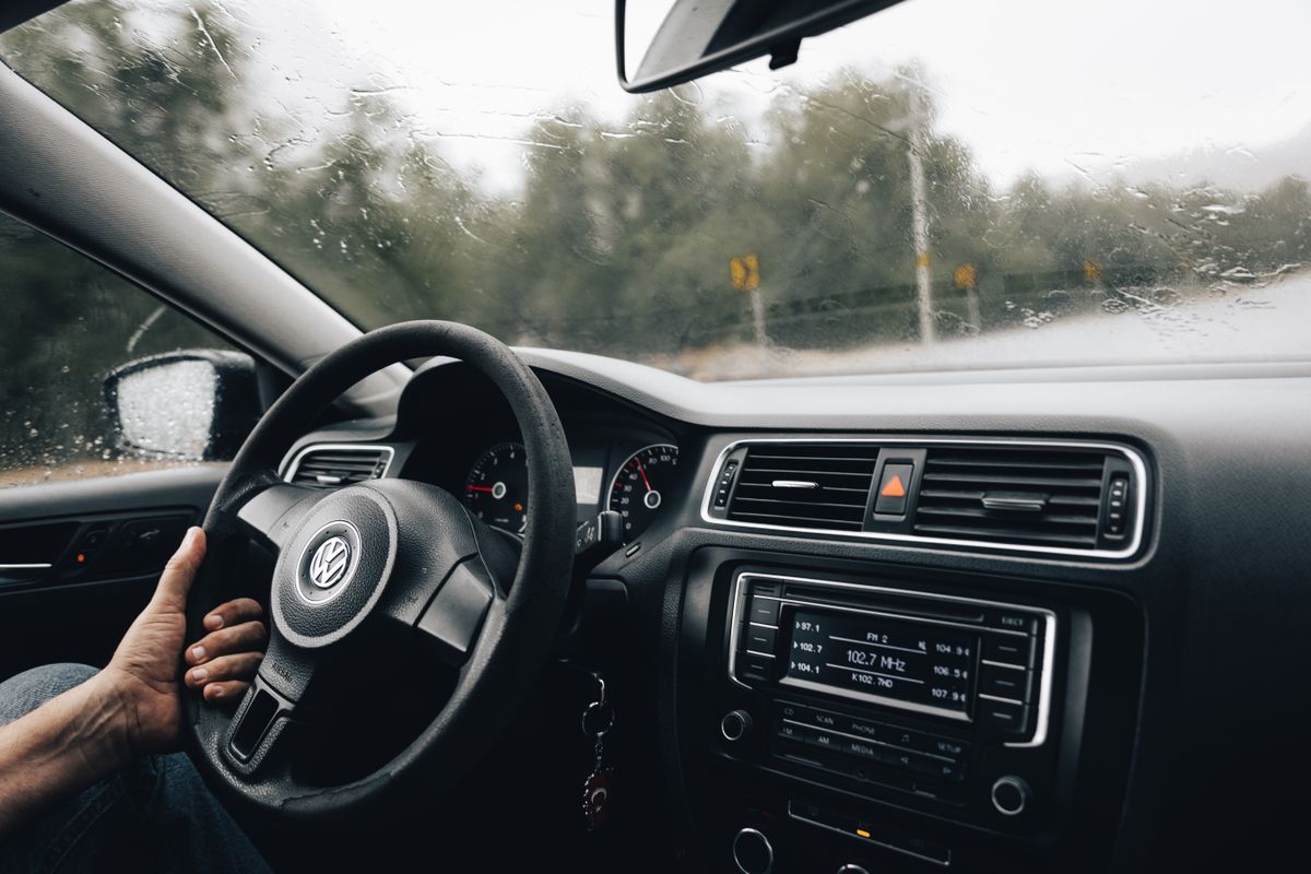 Interior view of a car dashboard and steering wheel on a rainy day journey.