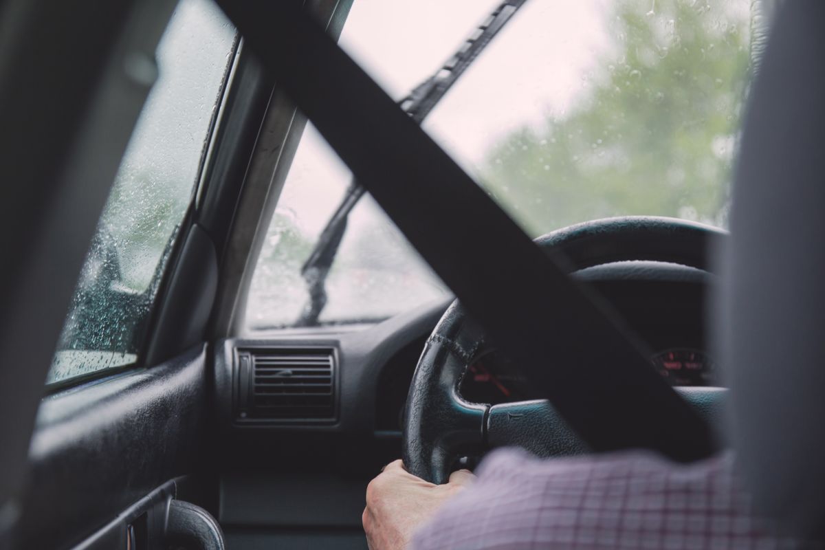 Interior view of a car during rainy weather, emphasizing safety with visible seat belt and driver focused on road.