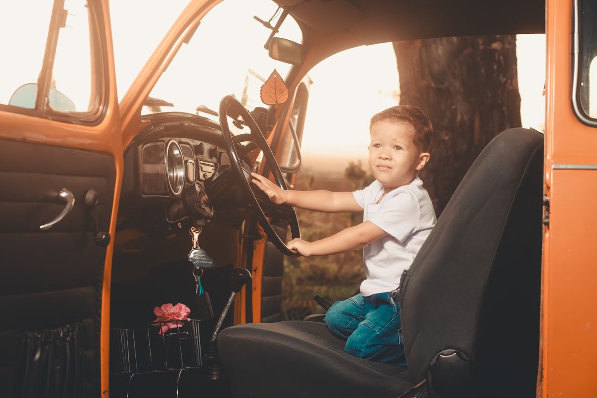 Child sits in vintage car, looking out, learned driving fun.