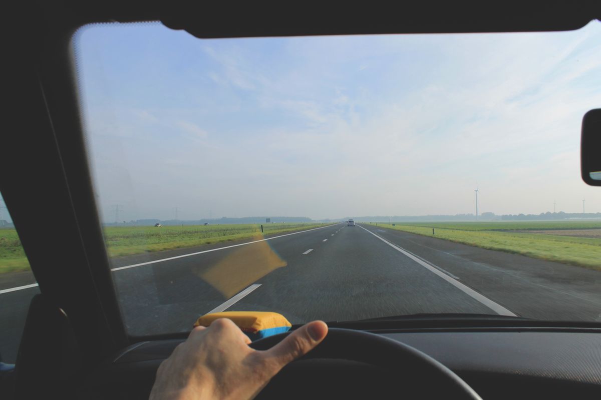 View from a car through the windshield, driving down an empty highway with clear skies and green fields.