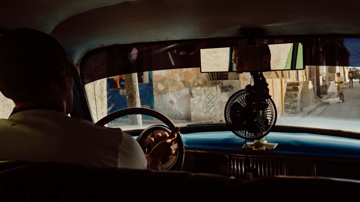 Driver in a vintage car navigating a scenic urban street with reflections.