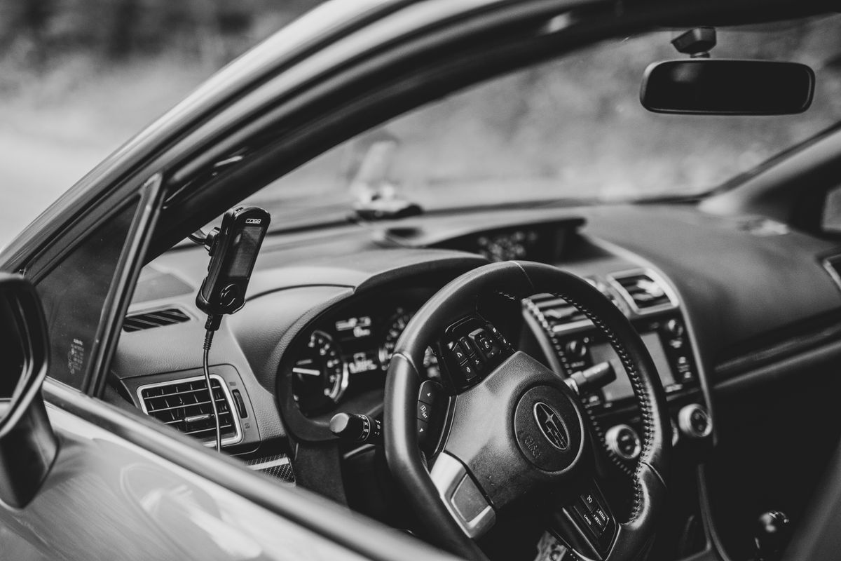 A monochrome view inside a modern car focusing on the steering wheel and dashboard technology.
