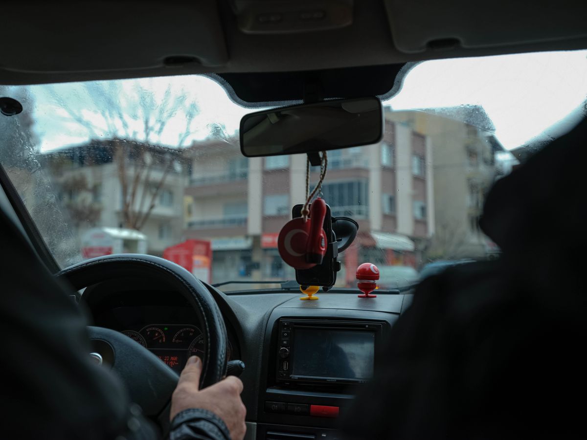 A driver's perspective of a car interior navigating through city streets with focus on the dashboard and rearview mirror.