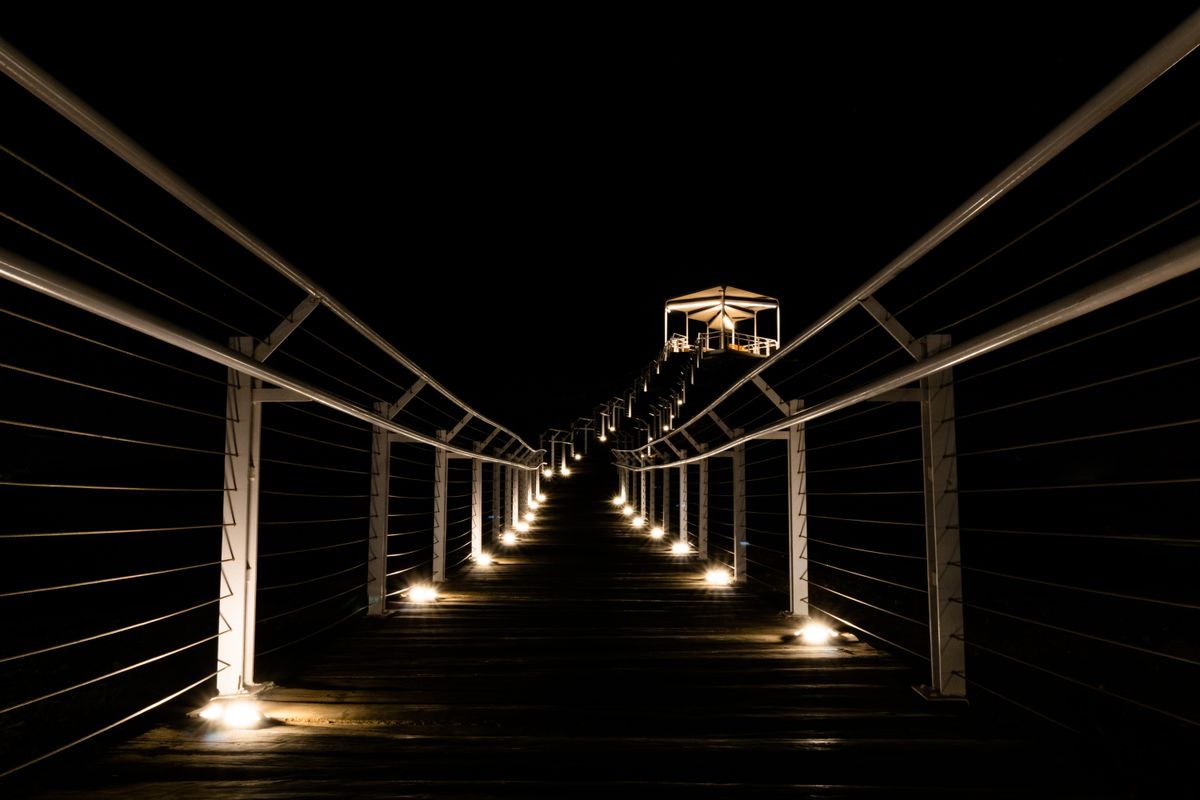 A captivating night view of an illuminated footbridge with railings leading to a gazebo.