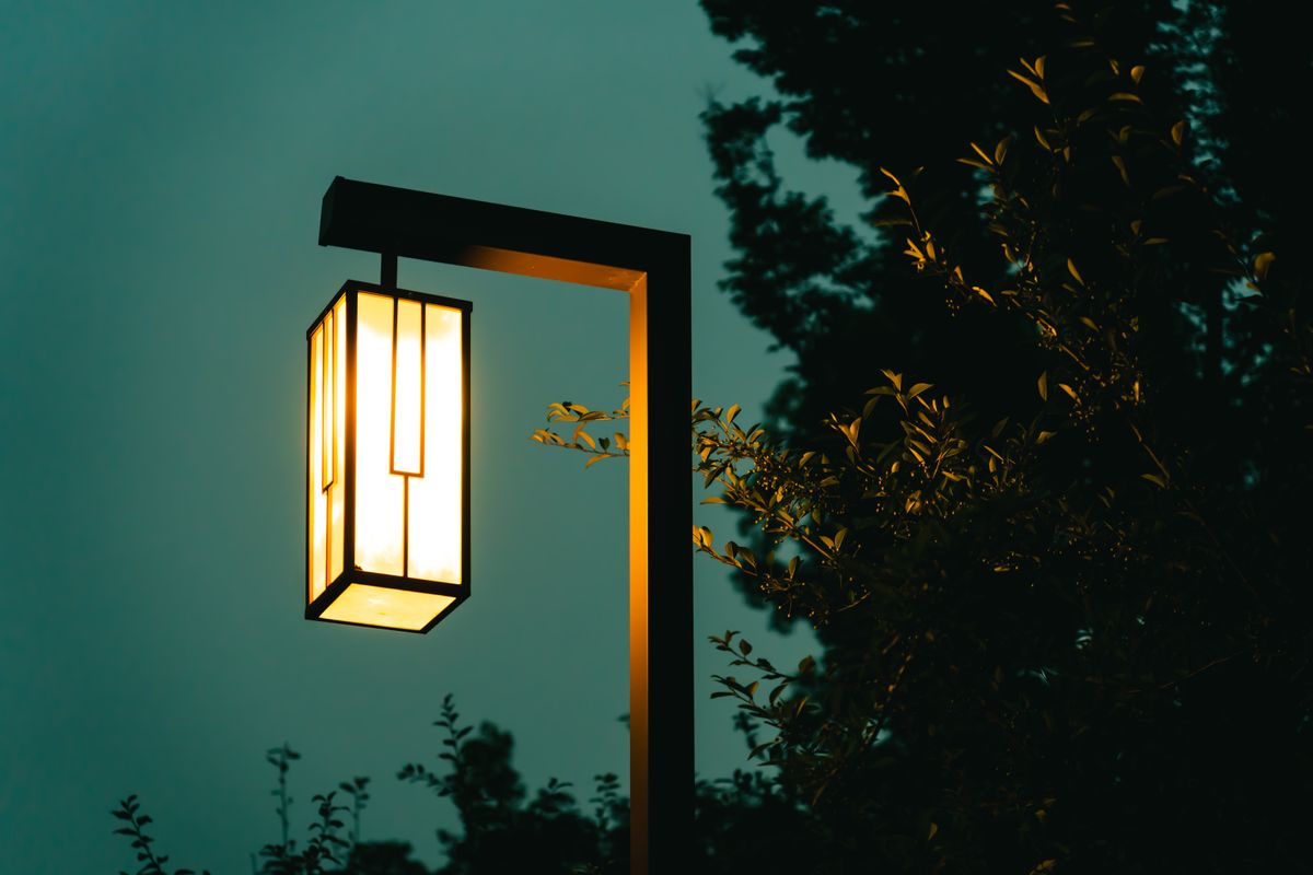 A glowing street lamp shines softly in an evening atmosphere surrounded by foliage.