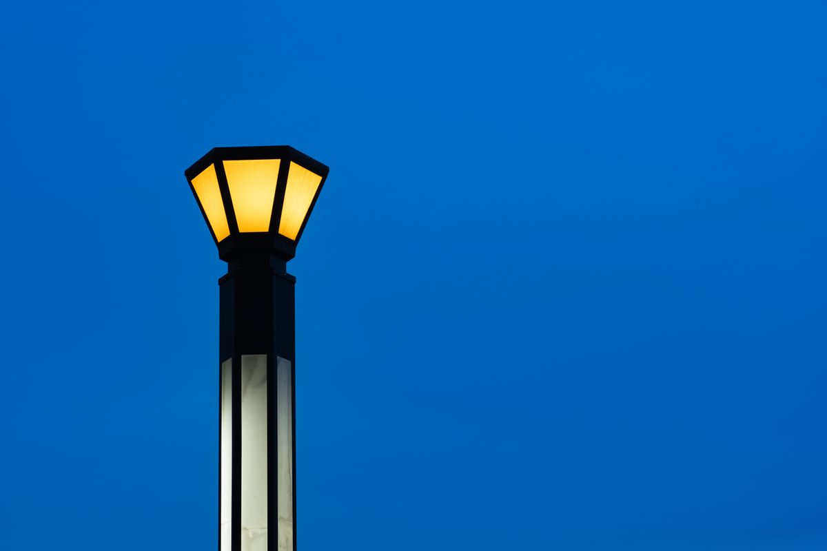 An illuminated streetlamp stands against a minimalist blue evening sky, creating a serene atmosphere.